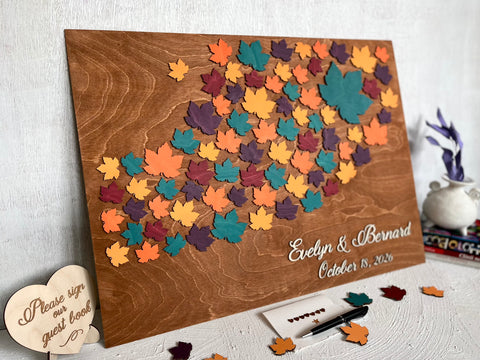Wooden board with colorful maple leaf-shaped cutouts and personalized  names and date- used as a wedding guest book alternative for guest signatures