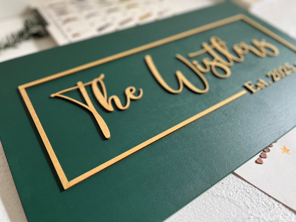 detail of personalized last name sign with established year made on dark green wood with gold lettering for wedding or office sign. The sign is rectangular and the font is calligraphic. You will personalize your sign with your name, year, color for the background, color for the text as well as font type. 