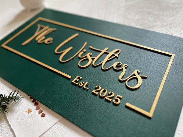 detail of personalized last name sign with established year made on dark green wood with gold lettering for wedding or office sign. The sign is rectangular and the font is calligraphic. You will personalize your sign with your name, year, color for the background, color for the text as well as font type. 