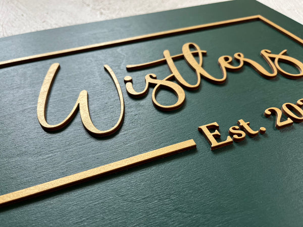 detail of personalized last name sign with established year made on dark green wood with gold lettering for wedding or office sign. The sign is rectangular and the font is calligraphic. You will personalize your sign with your name, year, color for the background, color for the text as well as font type. 