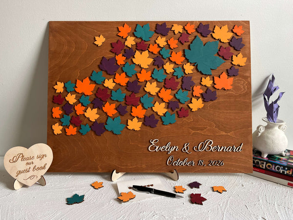 Wooden board with colorful maple leaf-shaped cutouts and personalized  names and date- used as a wedding guest book alternative for guest signatures