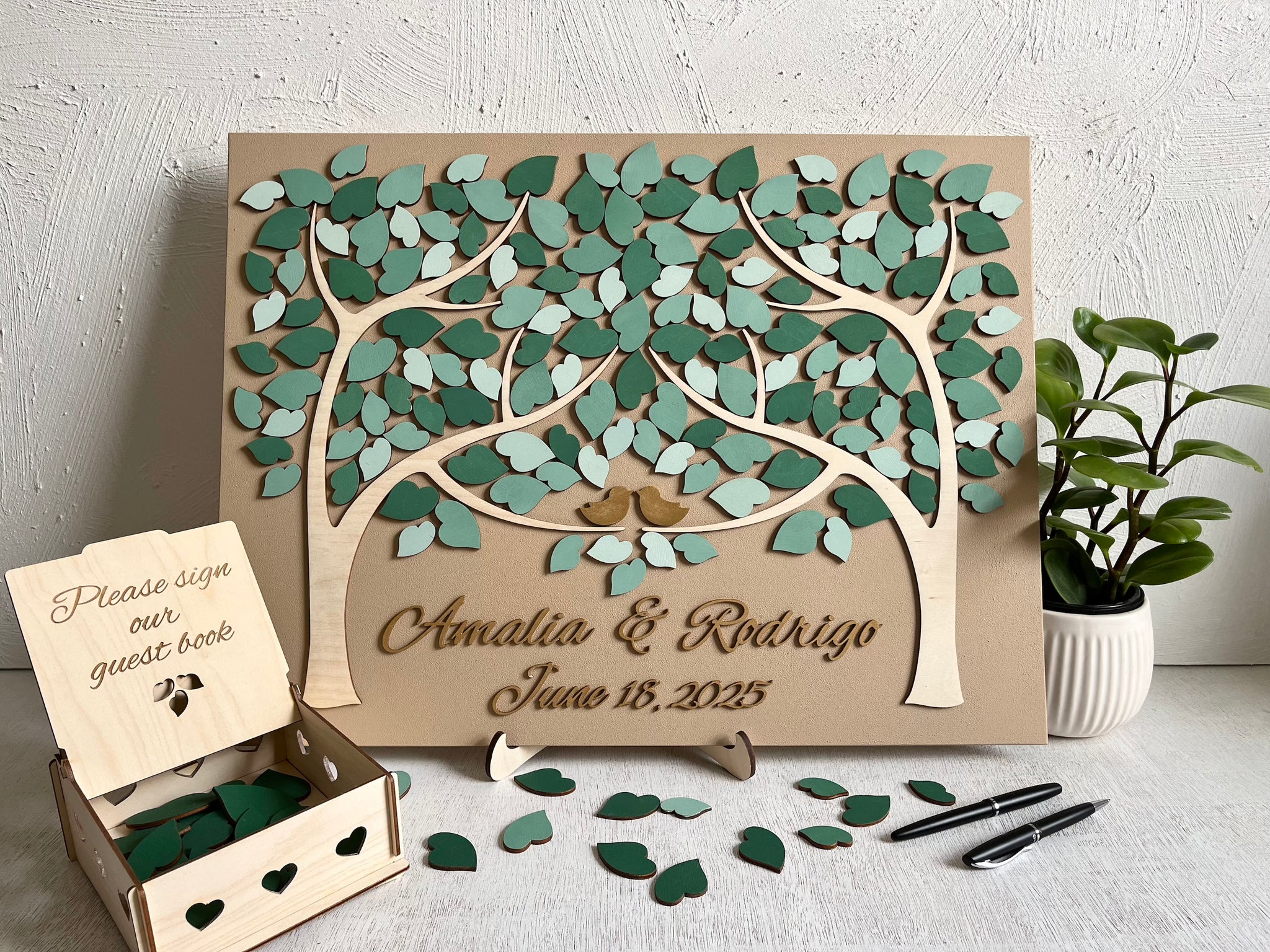 magnetic guest book for wedding made with two trees, personalized names and wedding date in gold font, magnetic leaves for guests to sign and a holder for the board plus a box for the leaves.