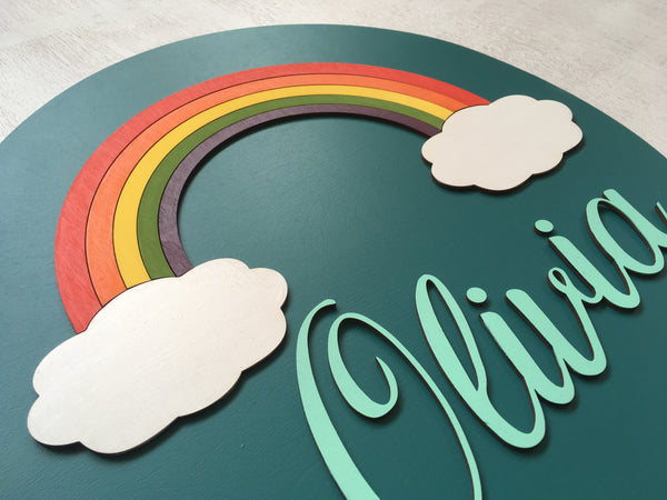 detail of round baby name sign with rainbow made on a teal background