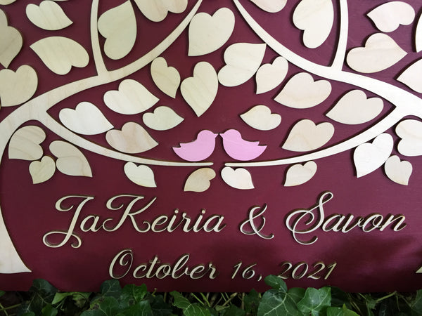the two trees come together to shelter the two birds that sit on the tree on top of the personalized names and wedding date on this custom guestbook